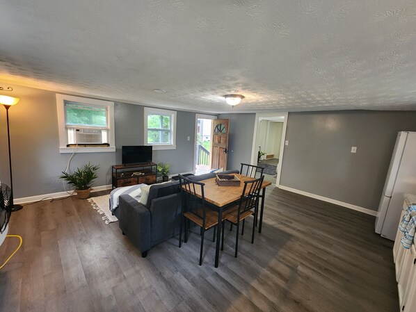 Una sala de estar moderna con un sofá gris, una mesa de comedor de madera y un televisor sobre un mueble.