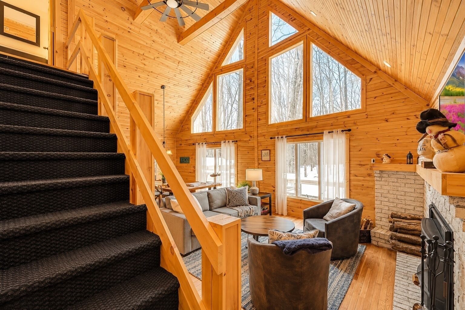 A spacious cabin interior with a wooden staircase, a fireplace, and a cozy seating area.