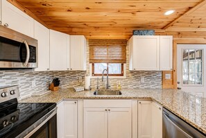 A modern kitchen with white cabinets, a granite countertop, stainless steel appliances, and a window with blinds. - Beautiful Lodge in The Hideout!! (Lake Ariel)