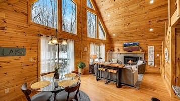 A cozy cabin interior with a dining area, kitchen, and living space, featuring wooden walls and large windows.