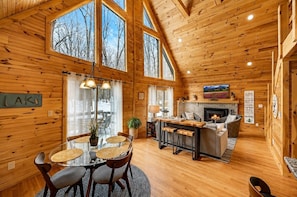 A cozy cabin interior with a dining area, kitchen, and living space, featuring wooden walls and large windows. - Beautiful Lodge in The Hideout!! (Lake Ariel)