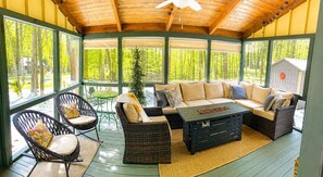 A covered outdoor seating area with wicker furniture, a coffee table, and a view of a forested area. - Beautiful Lodge in The Hideout!! (Lake Ariel)