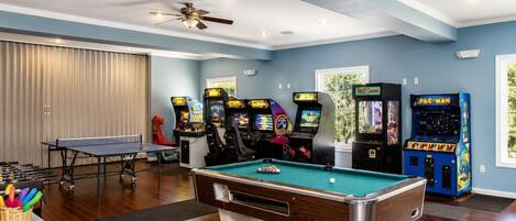 A recreational room with a pool table, arcade machines, and a ping pong table.