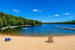 A sandy beach with a lifeguard chair, a clear blue sky, and a calm lake surrounded by trees. - Beautiful Lodge in The Hideout!! (Lake Ariel)