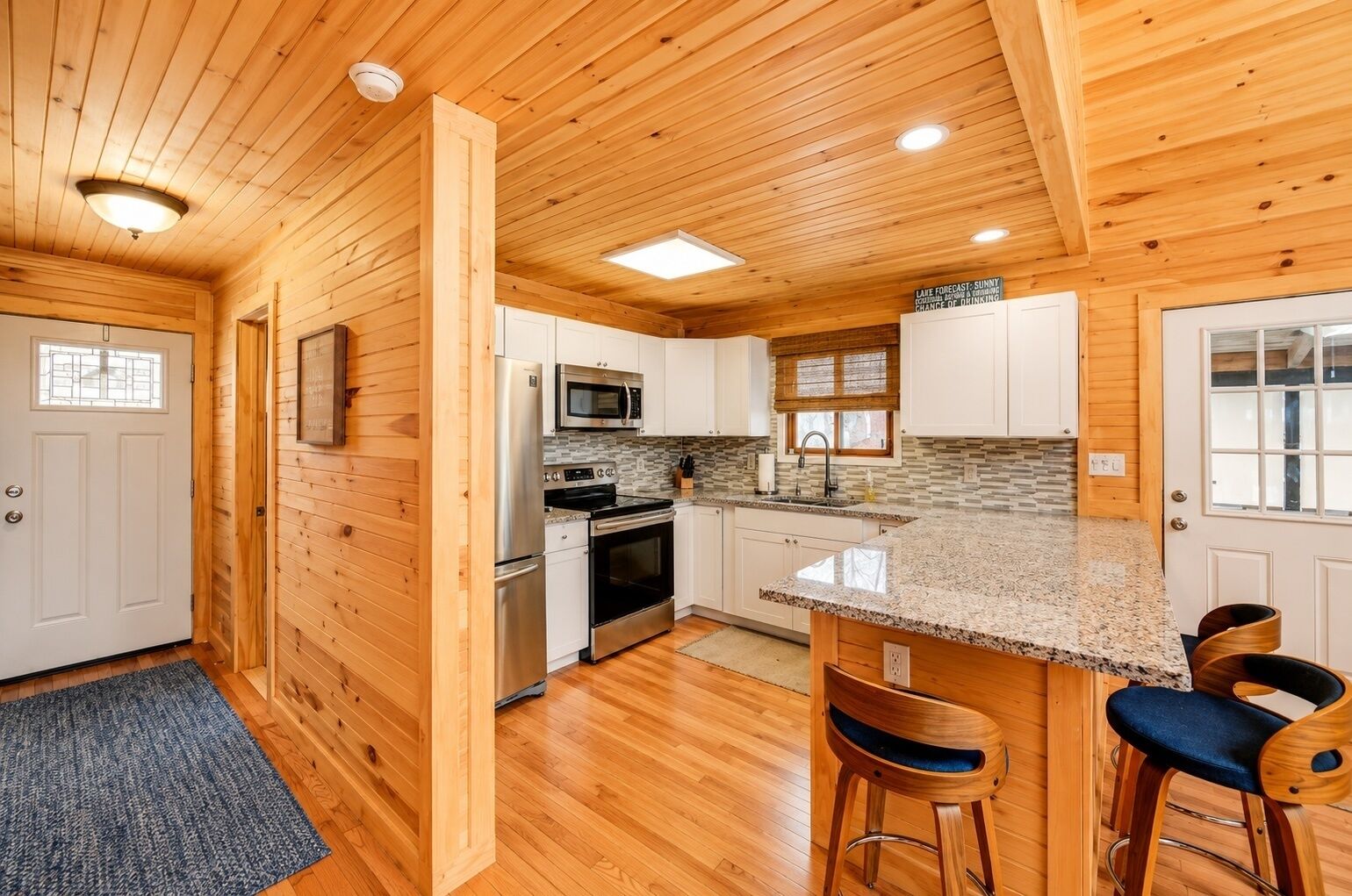 A kitchen with wooden walls, a granite countertop, stainless steel appliances, and a bar area with stools.