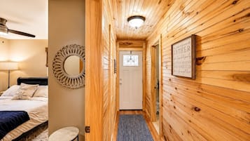 A wooden interior hallway with a bed, a round mirror, a framed sign, and a door.