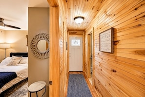 A wooden interior hallway with a bed, a round mirror, a framed sign, and a door. - Beautiful Lodge in The Hideout!! (Lake Ariel)