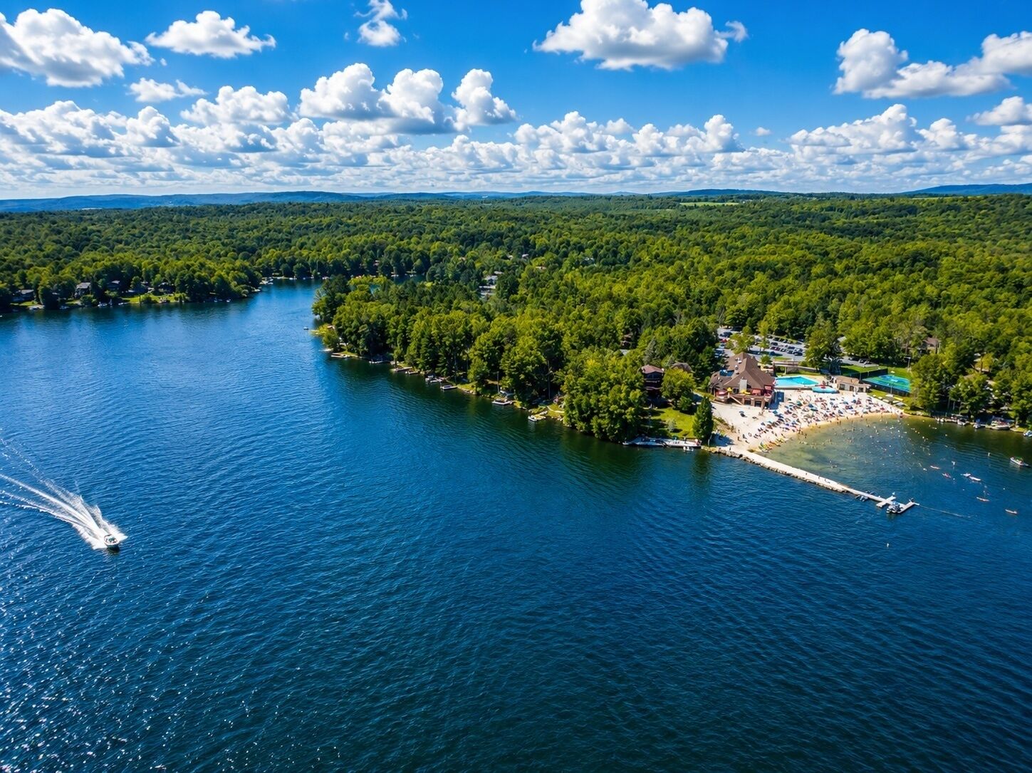 An aerial view of a lakeside resort with a beach, boat dock, and dense forest.