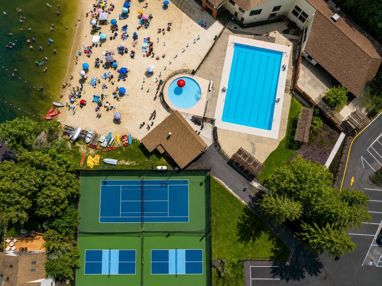An aerial view of a beach area with a swimming pool, a tennis court, and a building with a roof.