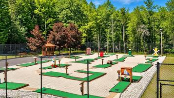 Un parcours de mini-golf avec plusieurs trous, un kiosque et une clôture délimitant la zone.