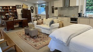 A modern bedroom with a large bed, a desk, a bookshelf, and a kitchen area.