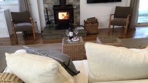 A cozy living room with a fireplace, two armchairs, a sofa, and a coffee table with a bottle and glass.
