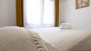 Una habitació d'hotel amb un llit, una finestra amb cortines, un aparell d'aire condicionat i una obra d'art penjada a la paret.