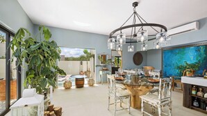 Un comedor espacioso con una mesa de cristal, sillas blancas y una planta grande.