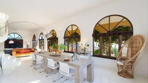 A spacious living area with a dining table, white chairs, a sofa, and a wicker chair.