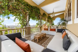 A sunlit outdoor seating area with a sofa and chairs, a table, and a view of the landscape.