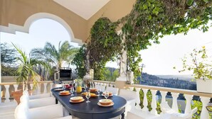 An outdoor dining area with a table set for four, surrounded by white chairs, overlooking a scenic view.
