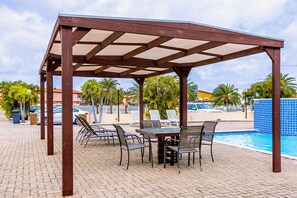 A covered outdoor seating area with a pool in the background. - 2BR Townhouse 3min walk 2 EagleBeach w/ Pool & BBQ (Oranjestad)