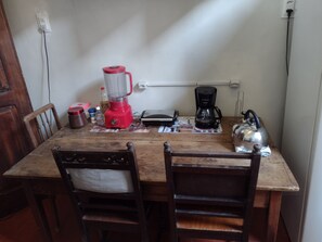 A wooden dining table with a red blender, a black coffee maker, and a kettle. There are chairs around the table. - Casa Rústica de Santa Teresa (Santa Teresa Rio de Janeiro)