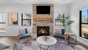 A modern living room with a stone fireplace, two sofas, a coffee table, and a TV mounted above the fireplace. - Luxury Property-Walk to lake and downtown Lake Geneva. Pet Friendly, Sleeps 8 (Lake Geneva)