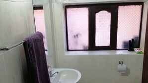 Une salle de bain avec un lavabo blanc, un miroir, une fenêtre à vitre dépolie et un tapis sur le sol.