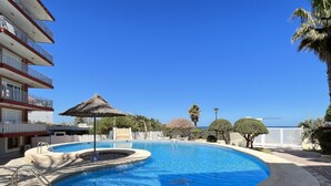 Ein Swimmingpool mit einer strohgedeckten Sonnenschirm, umgeben von einer Poolterrasse und einem Gebäude mit Balkonen.