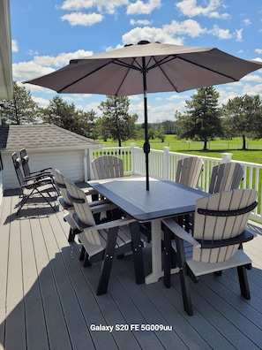 A deck with a Galaxy S20 FE 5G009uu table and chairs, an umbrella, and a view of the surrounding landscape.