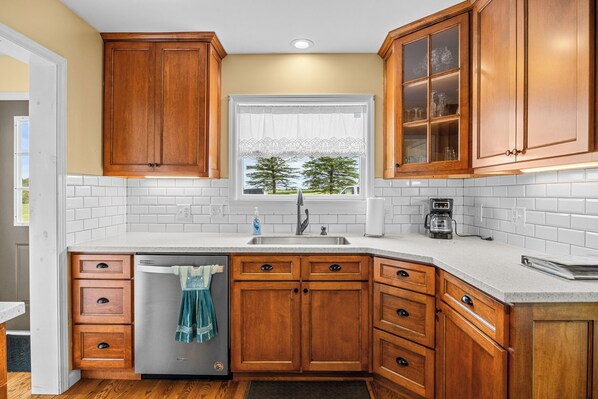 A kitchen with wooden cabinets, a stainless steel refrigerator, a window with a view of trees, and a coffee maker.