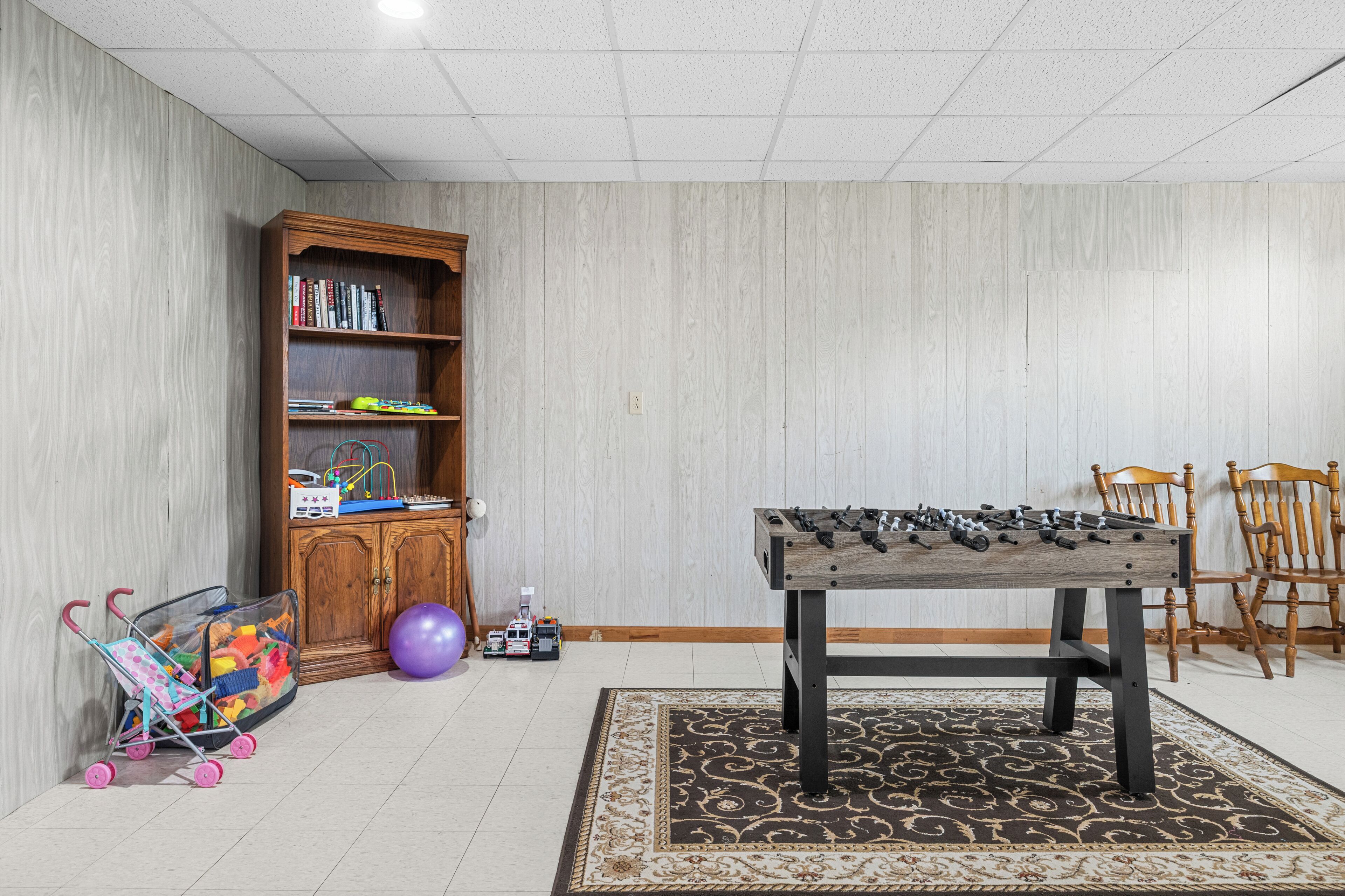 A room with a foosball table, a bookshelf, and a toy car.