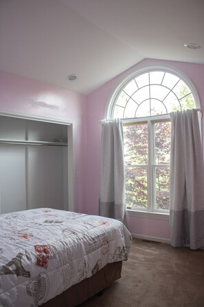 A bedroom with a bed, a window with curtains, and a closet.