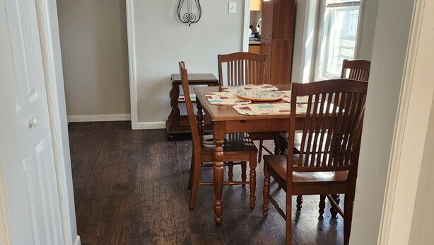 A dining area with a wooden table and chairs, a wall clock, and a window with blinds. - Irvington Apartment (Irvington)