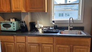 A kitchen with wooden cabinets, a built-in oven, a sink, and a window with a view of buildings. - Irvington Apartment (Irvington)