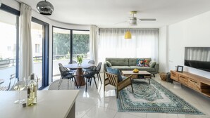 Ein modernes Wohnzimmer mit einer Couch, einem Esstisch, Stühlen, einem Fernseher und einem großen Fenster mit Vorhängen.