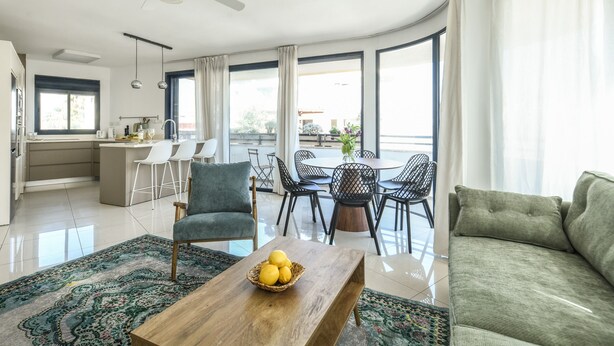 Ein modernes Wohnzimmer mit einem Holztisch, einem grünen Sofa und einem Essbereich mit rundem Tisch und Stühlen.