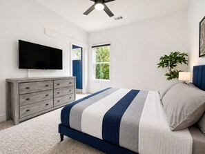 A bedroom with a bed, dresser, TV, windows, and a ceiling fan.