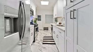 A modern kitchen with white cabinetry, stainless steel appliances, and a marble floor.