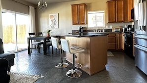 Een moderne keuken met een centraal eiland, houten kasten, roestvrijstalen apparatuur, en een eethoek met een tafel en stoelen.