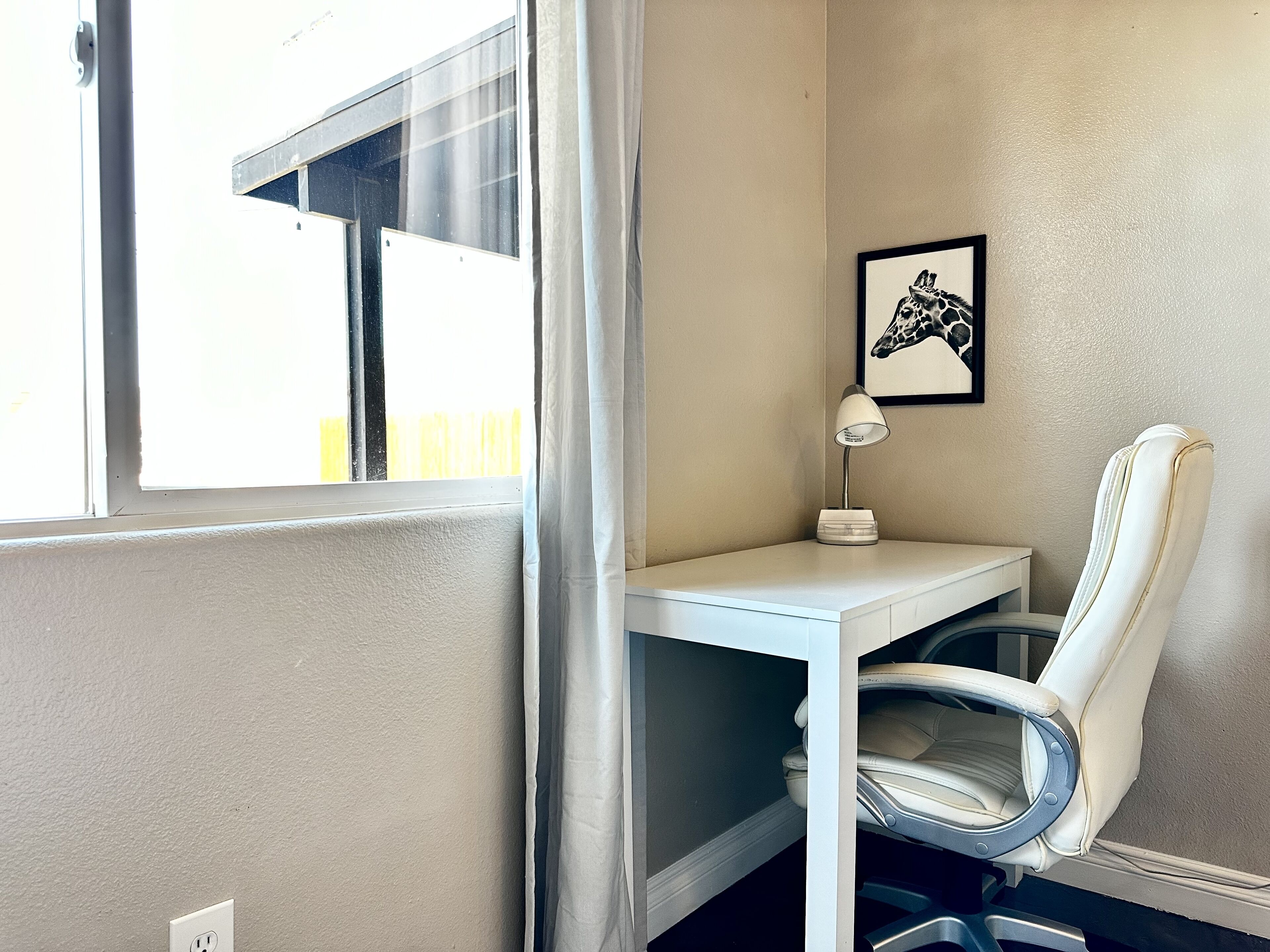 A corner office with a desk, chair, and a framed picture on the wall.
