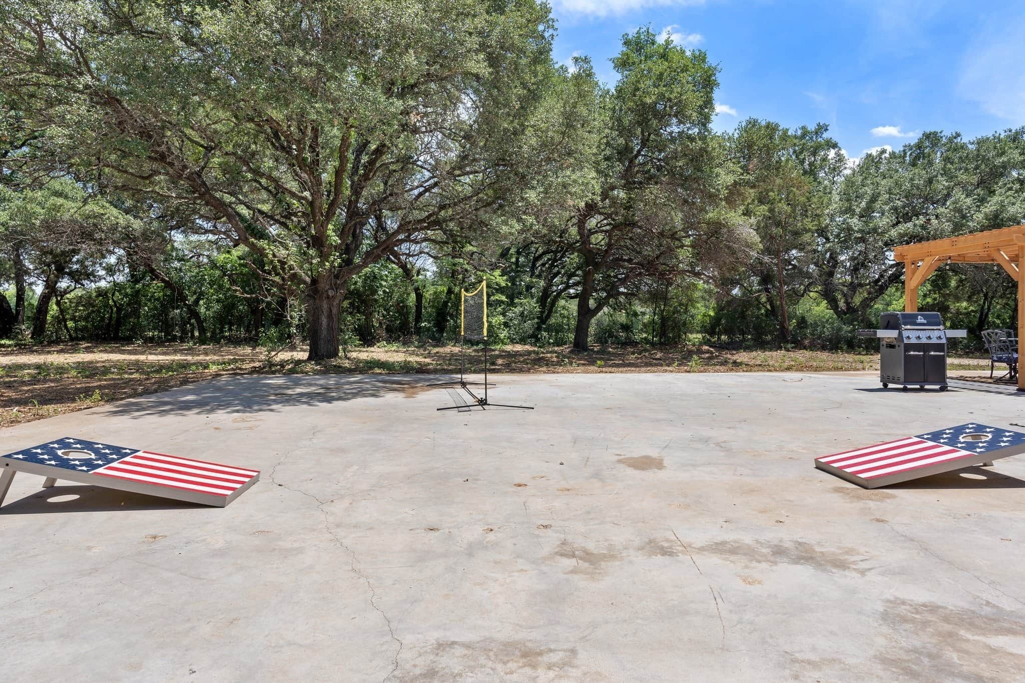 An outdoor area with a concrete floor, two American flag-themed chairs, a wooden pergola, and a barbecue grill.