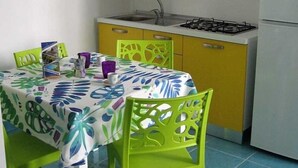 A small kitchen with yellow cabinets, a white refrigerator, and a table with a colorful tablecloth. - Studio with equipped kitchen - Pisciotta (Pisciotta)