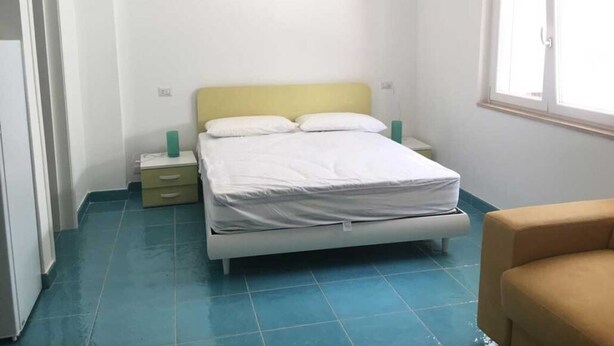 A bedroom with a bed, a nightstand, a chair, and a window. - Studio with equipped kitchen - Pisciotta (Pisciotta)
