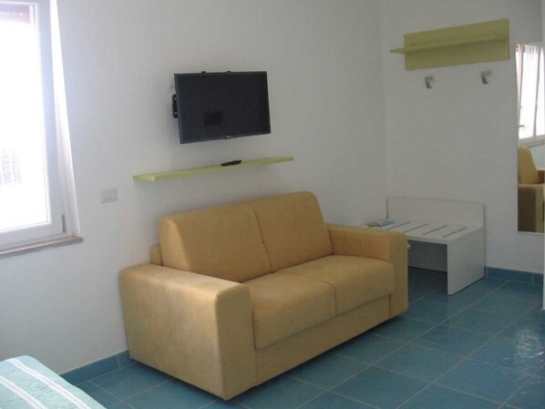 A room with a beige sofa, a flat-screen TV mounted on the wall, a small white table, and a window with a view.