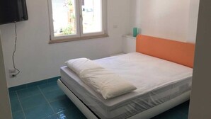 Une petite pièce avec un lit, une fenêtre et un téléviseur fixé au mur.