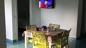 Un coin repas avec une table dressée pour quatre personnes, des chaises jaunes et un téléviseur fixé au mur.