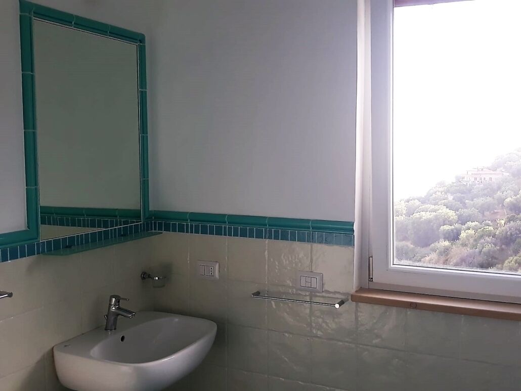 A bathroom with a sink, mirror, and window with a view of trees.