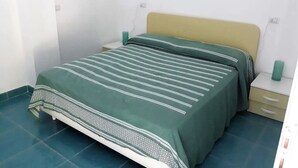 Un lit simple avec une couvre-lit à rayures vertes et blanches, une tête de lit beige et une table de chevet avec une lampe verte.