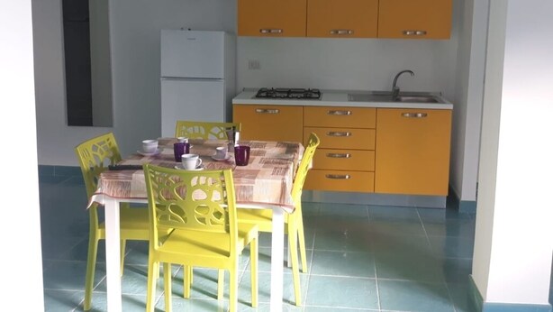 Une cuisine de taille réduite avec des meubles de couleur jaune, un réfrigérateur blanc et une cuisinière à gaz.