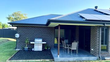 A modern house with a brick exterior, a covered patio with outdoor furniture, and a barbecue grill.