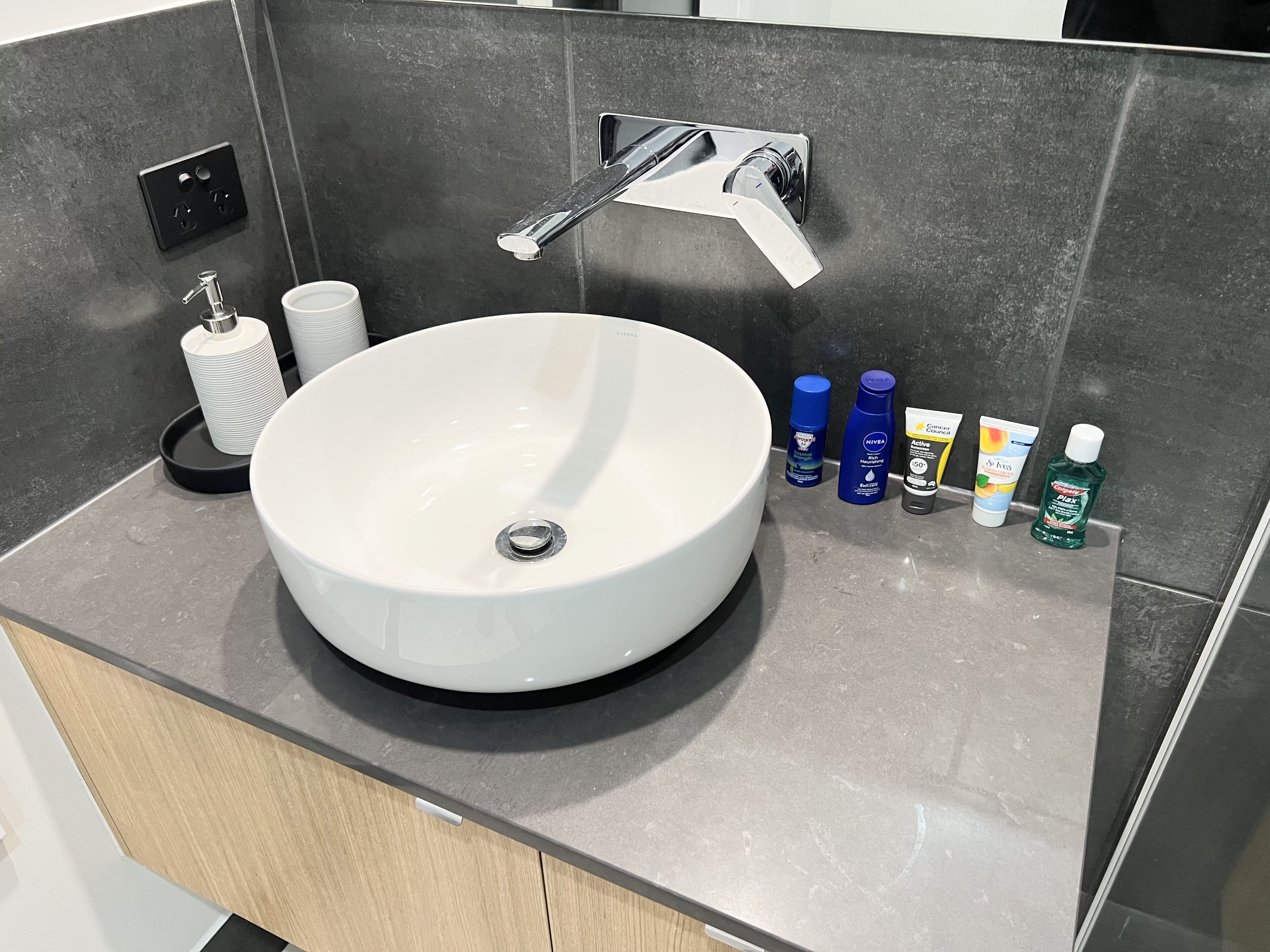 A modern bathroom with a large white sink, a chrome faucet, and a dark countertop.