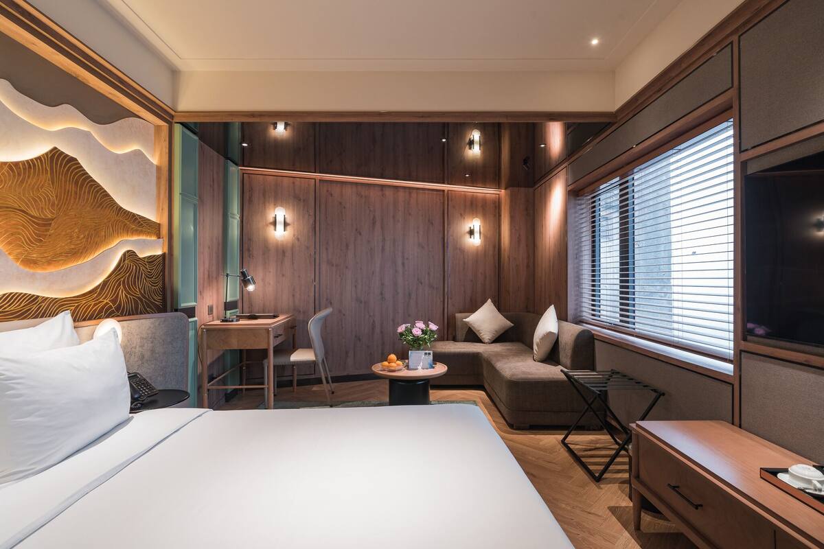 A modern hotel room with a bed, a desk, a chair, a sofa, and a TV.